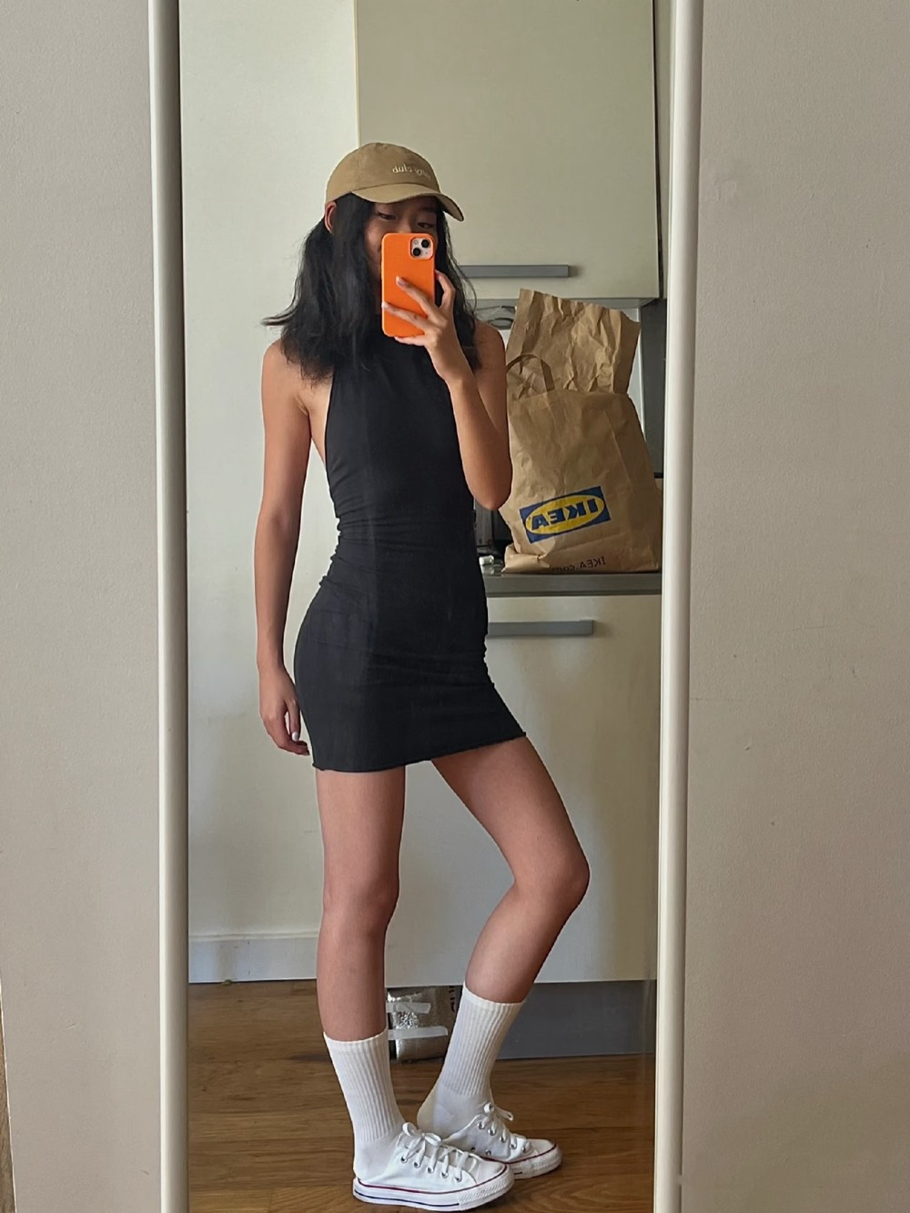 Black sleeveless mini dress with a tan baseball cap, white crew socks and white Converse